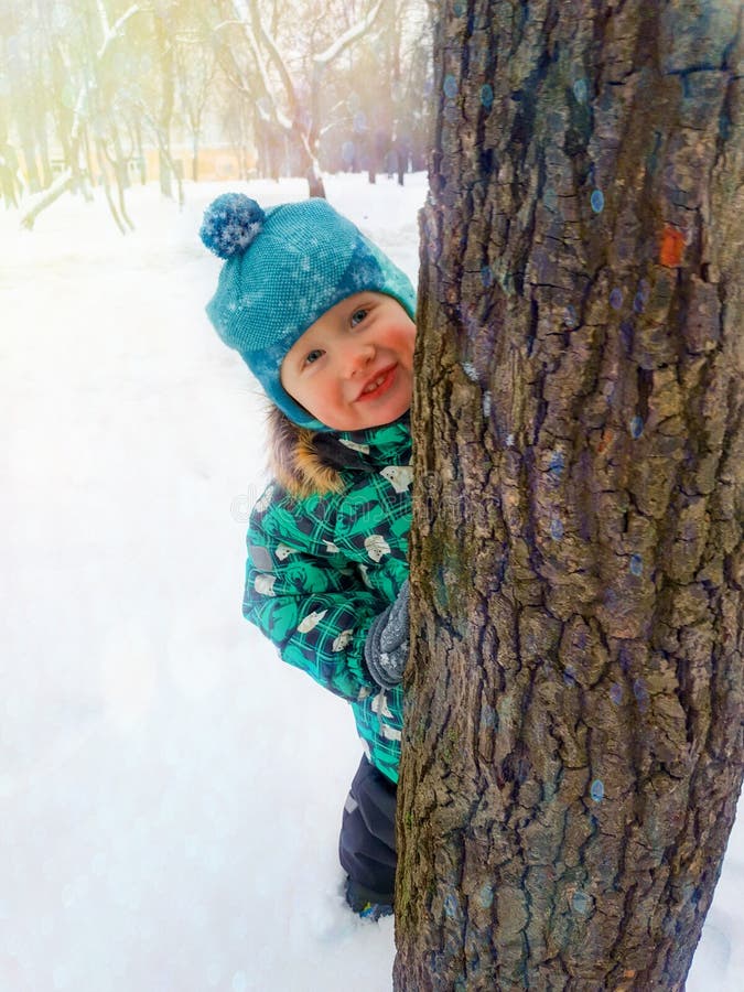 Мальчик счастливо усмехается peeking от позади ствола дерева на зимний день стоковое изображение Мальчик счастливо усмехается peeking от позади ствола дерева на зимний день стоковое изображение