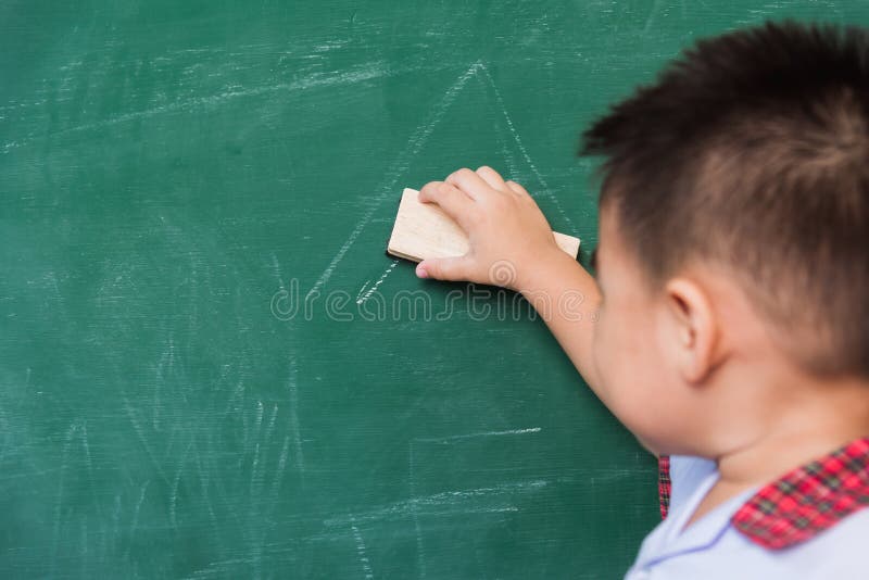 Back to School. Back of Asian cute little child boy kindergarten preschool in student uniform wiping clean or erase chalk on green school blackboard with sponge, First time to school education concept. Back to School. Back of Asian cute little child boy kindergarten preschool in student uniform wiping clean or erase chalk on green school blackboard with sponge, First time to school education concept