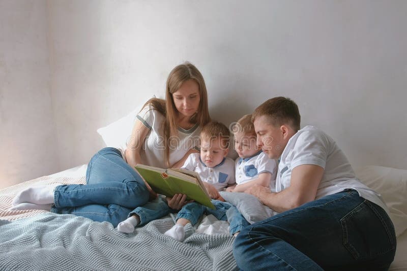 Мама семьи, папа и 2 брат-близнеца прочитали книги кладя на кровать Время чтения семьи стоковое изображение rf Мама семьи, папа и 2 брат-близнеца прочитали книги кладя на кровать Время чтения семьи стоковое изображение rf