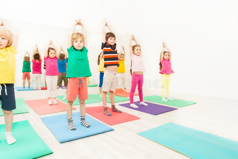 Group of 5-6 years old kids standing on yoga mats with their hands up during gymnastics in sport club. Group of 5-6 years old kids standing on yoga mats with their hands up during gymnastics in sport club