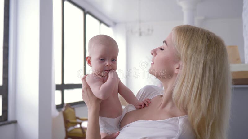 Материнская нежность, любя мать прижимаясь newborn ребенок на руках и нежно целуя ее дома