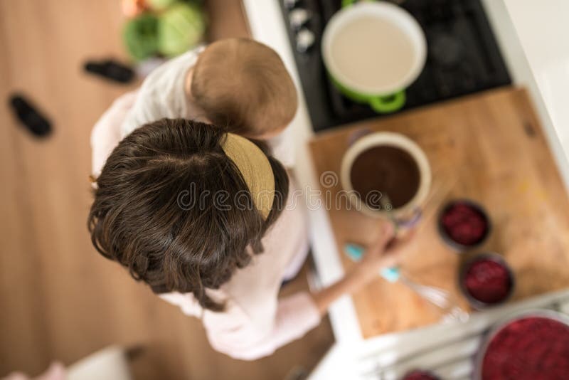 Мать держа ее младенца в одной руке делая очень вкусные торты с другим стоковые изображения