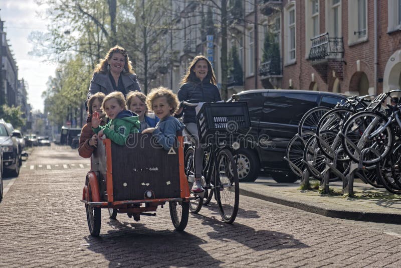 A mother with a bike and carrier with four kids bicycling down the street in Amsterdam. A mother with a bike and carrier with four kids bicycling down the street in Amsterdam.
