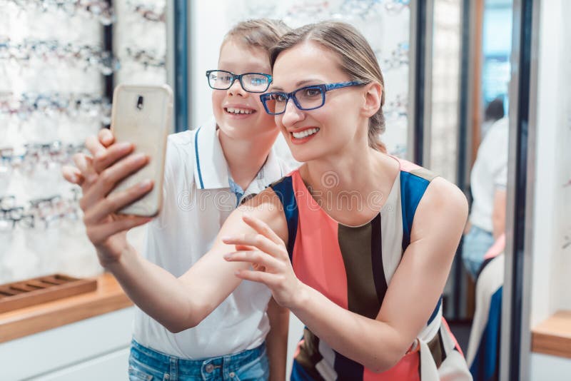 Mother and son taking selfie with new glasses at optometrist shop being happy. Mother and son taking selfie with new glasses at optometrist shop being happy