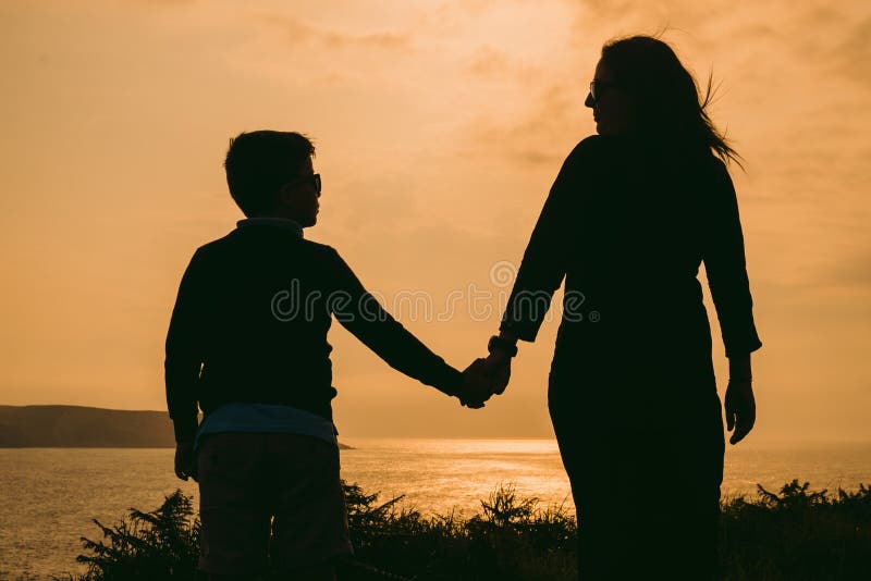 Mother and son on sunset holding by hands, outside isolated in front of a sunset in the sky on a summer day. Mother and son on sunset holding by hands, outside isolated in front of a sunset in the sky on a summer day