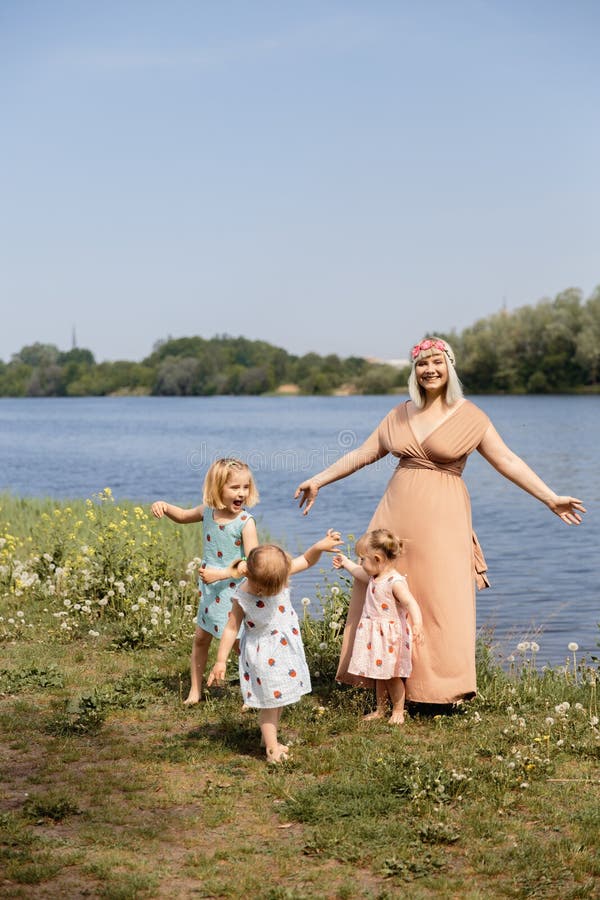 Mother having quality funny playing time with her baby girls at a park blowing dandelion - Young blonde hippie - Daughters wear similar dresses with strawberry print - Family values - 1, 2, 6 year old children on a sunny spring day. Mother having quality funny playing time with her baby girls at a park blowing dandelion - Young blonde hippie - Daughters wear similar dresses with strawberry print - Family values - 1, 2, 6 year old children on a sunny spring day