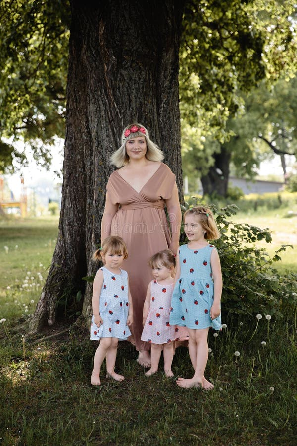 Mother having quality funny playing time with her baby girls at a park blowing dandelion - Young blonde hippie - Daughters wear similar dresses with strawberry print - Family values - 1, 2, 6 year old children on a sunny spring day. Mother having quality funny playing time with her baby girls at a park blowing dandelion - Young blonde hippie - Daughters wear similar dresses with strawberry print - Family values - 1, 2, 6 year old children on a sunny spring day