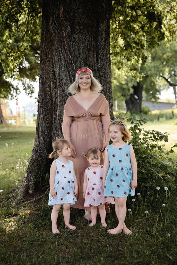 Mother having quality funny playing time with her baby girls at a park blowing dandelion - Young blonde hippie - Daughters wear similar dresses with strawberry print - Family values - 1, 2, 6 year old children on a sunny spring day. Mother having quality funny playing time with her baby girls at a park blowing dandelion - Young blonde hippie - Daughters wear similar dresses with strawberry print - Family values - 1, 2, 6 year old children on a sunny spring day