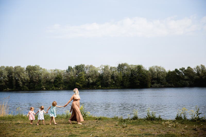 Mother having quality funny playing time with her baby girls at a park blowing dandelion - Young blonde hippie - Daughters wear similar dresses with strawberry print - Family values - 1, 2, 6 year old children on a sunny spring day. Mother having quality funny playing time with her baby girls at a park blowing dandelion - Young blonde hippie - Daughters wear similar dresses with strawberry print - Family values - 1, 2, 6 year old children on a sunny spring day