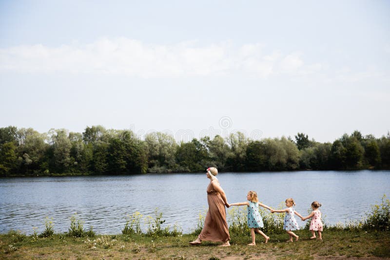 Mother having quality funny playing time with her baby girls at a park blowing dandelion - Young blonde hippie - Daughters wear similar dresses with strawberry print - Family values - 1, 2, 6 year old children on a sunny spring day. Mother having quality funny playing time with her baby girls at a park blowing dandelion - Young blonde hippie - Daughters wear similar dresses with strawberry print - Family values - 1, 2, 6 year old children on a sunny spring day