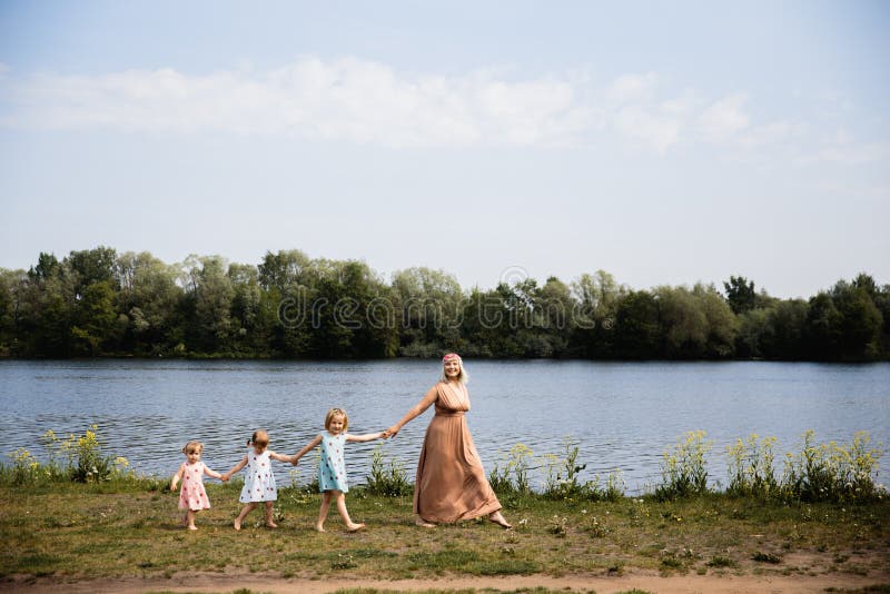 Mother having quality funny playing time with her baby girls at a park blowing dandelion - Young blonde hippie - Daughters wear similar dresses with strawberry print - Family values - 1, 2, 6 year old children on a sunny spring day. Mother having quality funny playing time with her baby girls at a park blowing dandelion - Young blonde hippie - Daughters wear similar dresses with strawberry print - Family values - 1, 2, 6 year old children on a sunny spring day