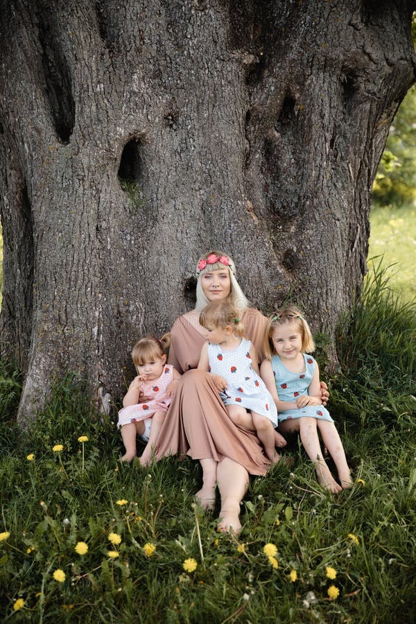 Mother having quality funny playing time with her baby girls at a park blowing dandelion - Young blonde hippie - Daughters wear similar dresses with strawberry print - Family values - 1, 2, 6 year old children on a sunny spring day. Mother having quality funny playing time with her baby girls at a park blowing dandelion - Young blonde hippie - Daughters wear similar dresses with strawberry print - Family values - 1, 2, 6 year old children on a sunny spring day