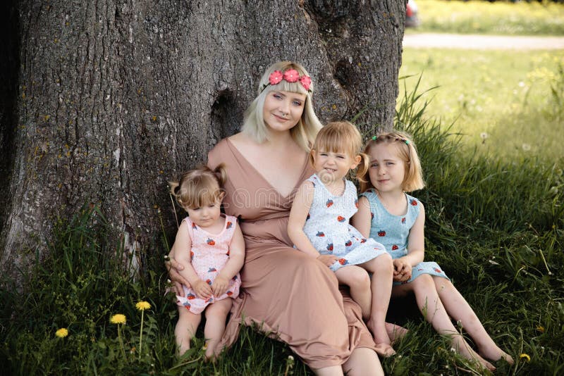 Mother having quality funny playing time with her baby girls at a park blowing dandelion - Young blonde hippie - Daughters wear similar dresses with strawberry print - Family values - 1, 2, 6 year old children on a sunny spring day. Mother having quality funny playing time with her baby girls at a park blowing dandelion - Young blonde hippie - Daughters wear similar dresses with strawberry print - Family values - 1, 2, 6 year old children on a sunny spring day