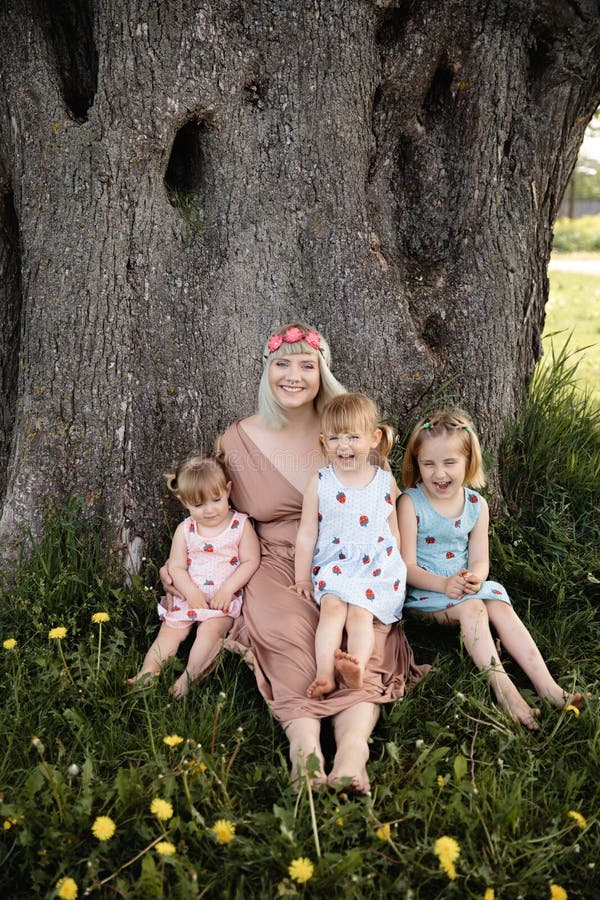 Mother having quality funny playing time with her baby girls at a park blowing dandelion - Young blonde hippie - Daughters wear similar dresses with strawberry print - Family values - 1, 2, 6 year old children on a sunny spring day. Mother having quality funny playing time with her baby girls at a park blowing dandelion - Young blonde hippie - Daughters wear similar dresses with strawberry print - Family values - 1, 2, 6 year old children on a sunny spring day