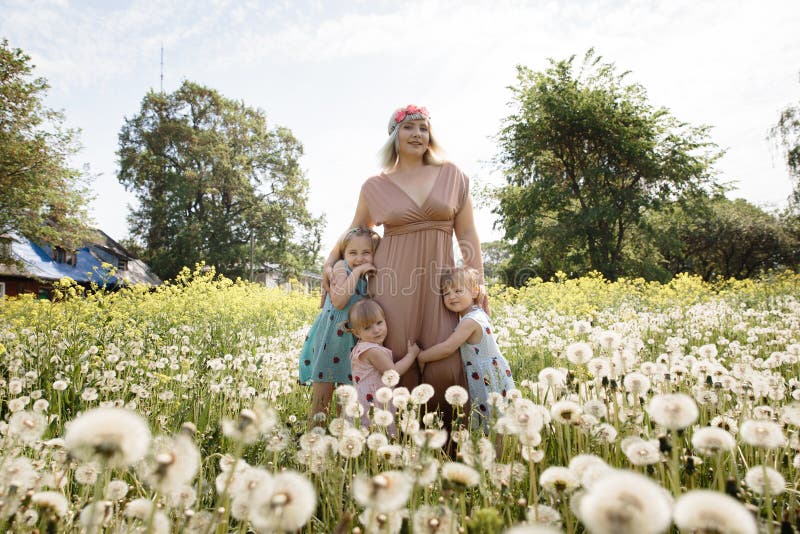 Mother having quality funny playing time with her baby girls at a park blowing dandelion - Young blonde hippie - Daughters wear similar dresses with strawberry print - Family values - 1, 2, 6 year old children on a sunny spring day. Mother having quality funny playing time with her baby girls at a park blowing dandelion - Young blonde hippie - Daughters wear similar dresses with strawberry print - Family values - 1, 2, 6 year old children on a sunny spring day