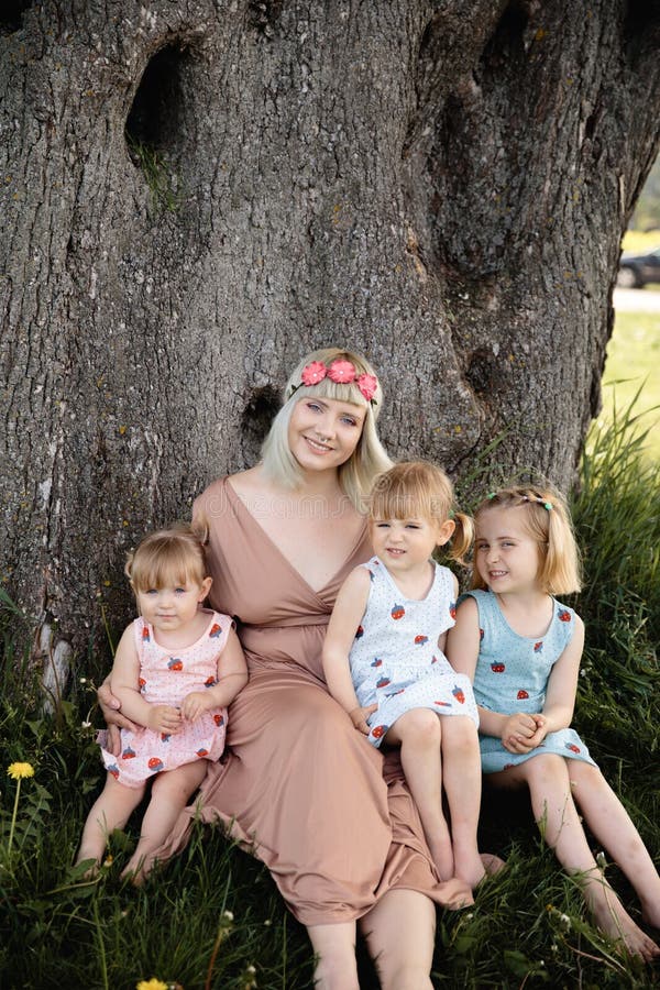 Mother having quality funny playing time with her baby girls at a park blowing dandelion - Young blonde hippie - Daughters wear similar dresses with strawberry print - Family values - 1, 2, 6 year old children on a sunny spring day. Mother having quality funny playing time with her baby girls at a park blowing dandelion - Young blonde hippie - Daughters wear similar dresses with strawberry print - Family values - 1, 2, 6 year old children on a sunny spring day