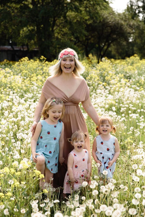 Mother having quality funny playing time with her baby girls at a park blowing dandelion - Young blonde hippie - Daughters wear similar dresses with strawberry print - Family values - 1, 2, 6 year old children on a sunny spring day. Mother having quality funny playing time with her baby girls at a park blowing dandelion - Young blonde hippie - Daughters wear similar dresses with strawberry print - Family values - 1, 2, 6 year old children on a sunny spring day