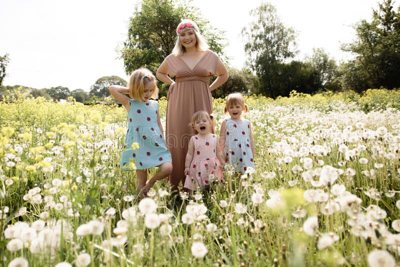 Mother having quality funny playing time with her baby girls at a park blowing dandelion - Young blonde hippie - Daughters wear similar dresses with strawberry print - Family values - 1, 2, 6 year old children on a sunny spring day. Mother having quality funny playing time with her baby girls at a park blowing dandelion - Young blonde hippie - Daughters wear similar dresses with strawberry print - Family values - 1, 2, 6 year old children on a sunny spring day