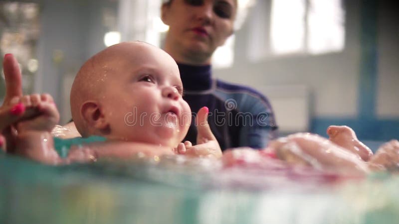 Мать или плавая тренер держат ребенка над водой и водят его через поверхность в бассейне держа руки видеоматериал