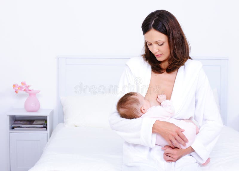 Young mother feeding her little baby with breast at home - indoors. Young mother feeding her little baby with breast at home - indoors