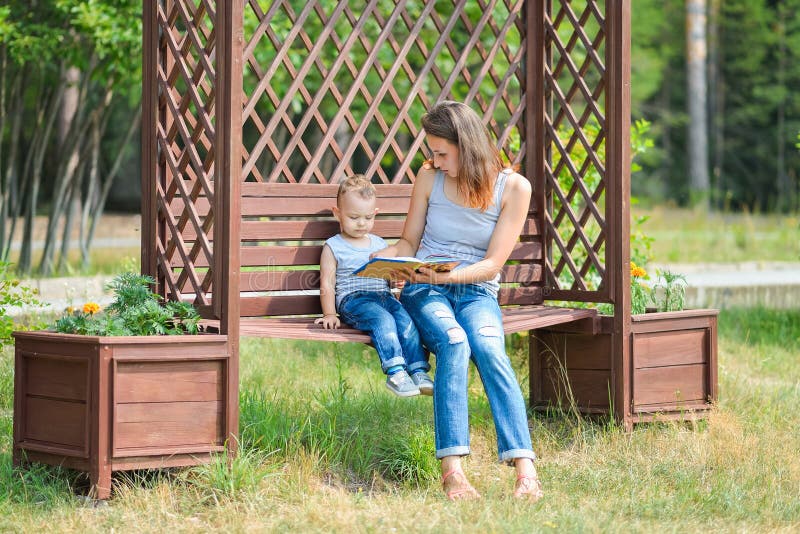 Мать при сын сидя на стенде в книге парка и чтения стоковые изображения rf Мать при сын сидя на стенде в книге парка и чтения стоковые изображения rf