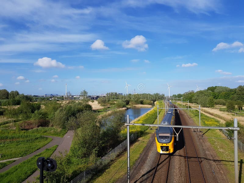 Междугородний поезд на железнодорожном пути с компенсацией природы и ветротурбины производящ зеленую энергию стоковое фото rf Междугородний поезд на железнодорожном пути с компенсацией природы и ветротурбины производящ зеленую энергию стоковое фото rf