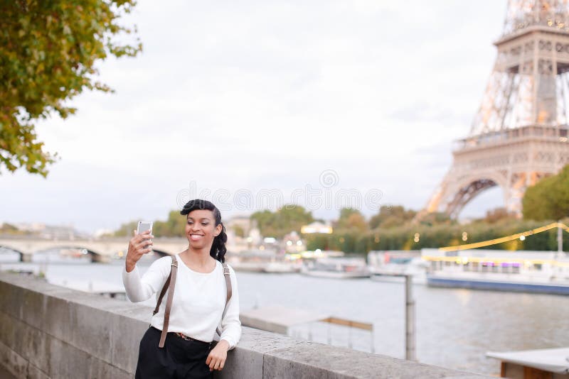Международный черный студент идя около Эйфелева башни и Сены и делая selfie smartphone, в Париже стоковое изображение rf Международный черный студент идя около Эйфелева башни и Сены и делая selfie smartphone, в Париже стоковое изображение rf