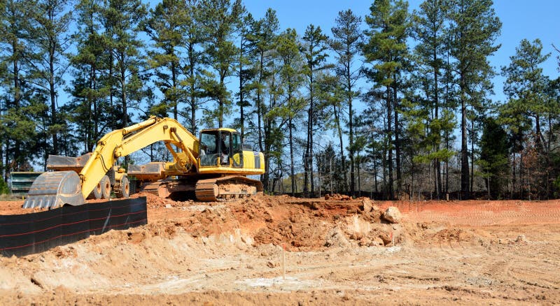 Yellow excavator moving red dirt in a construction site. Yellow excavator moving red dirt in a construction site.