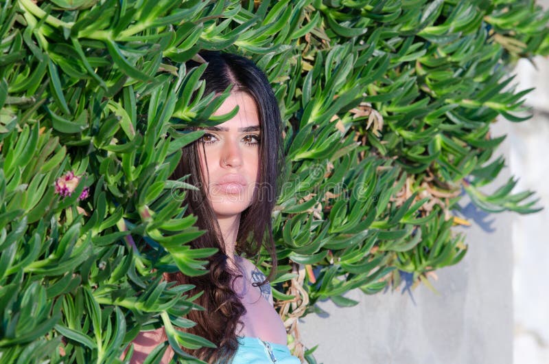Pretty lady with fleshy lips and long brunette hair, leaning against bush wall,facing the camera enjoying the sun on her face, horizontal photo. Pretty lady with fleshy lips and long brunette hair, leaning against bush wall,facing the camera enjoying the sun on her face, horizontal photo