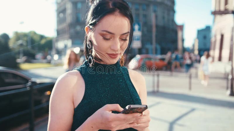 Милая девушка брюнет dreamily смотря на ее сообщении экрана мобильного телефона, прелестно усмехаться и отправки СМС пока стоящ в видеоматериал Милая девушка брюнет dreamily смотря на ее сообщении экрана мобильного телефона, прелестно усмехаться и отправки СМС пока стоящ в видеоматериал