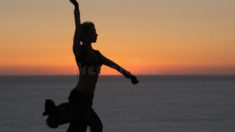 Милая маленькая девочка танцуя восточный танец на заходе солнца