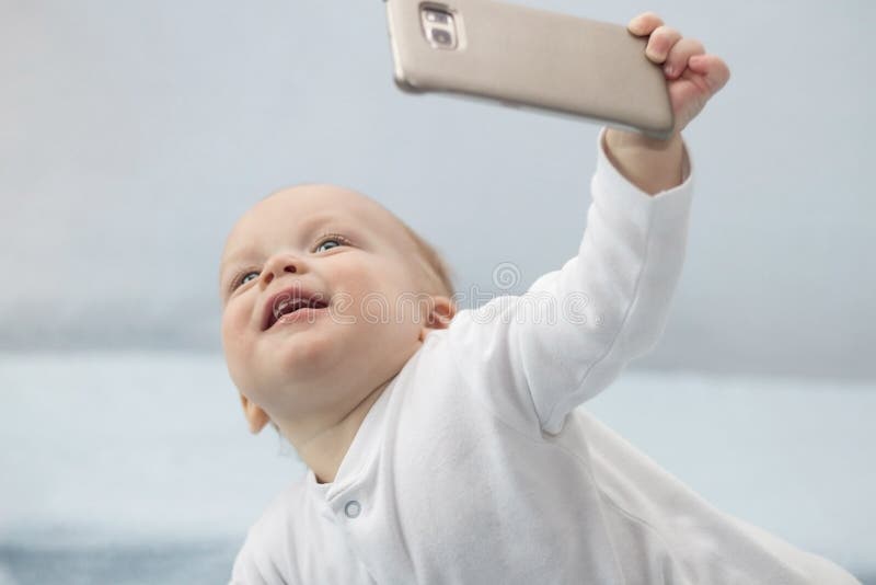 Милый младенческий мальчик делает selfie с сотовым телефоном Прелестный усмехаясь ребенк малыша принимая фото selfie с smartphone стоковые изображения rf Милый младенческий мальчик делает selfie с сотовым телефоном Прелестный усмехаясь ребенк малыша принимая фото selfie с smartphone стоковые изображения rf
