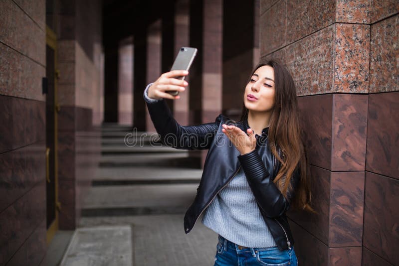 Милая молодая женщина имея прогулку и делая selfie около здания на улице стоковое изображение