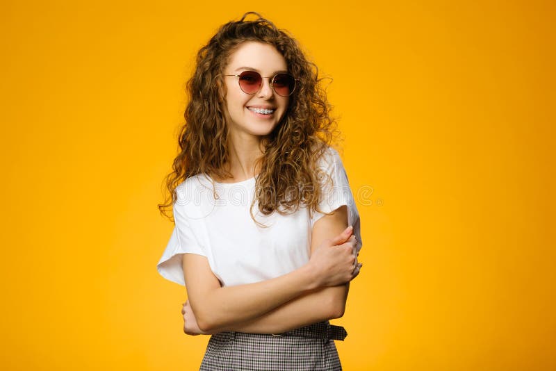 Pretty teenager wearing sunglasses and white shirt and looking at camera. Model isolated on colorful yellow background with copy space. Pretty teenager wearing sunglasses and white shirt and looking at camera. Model isolated on colorful yellow background with copy space