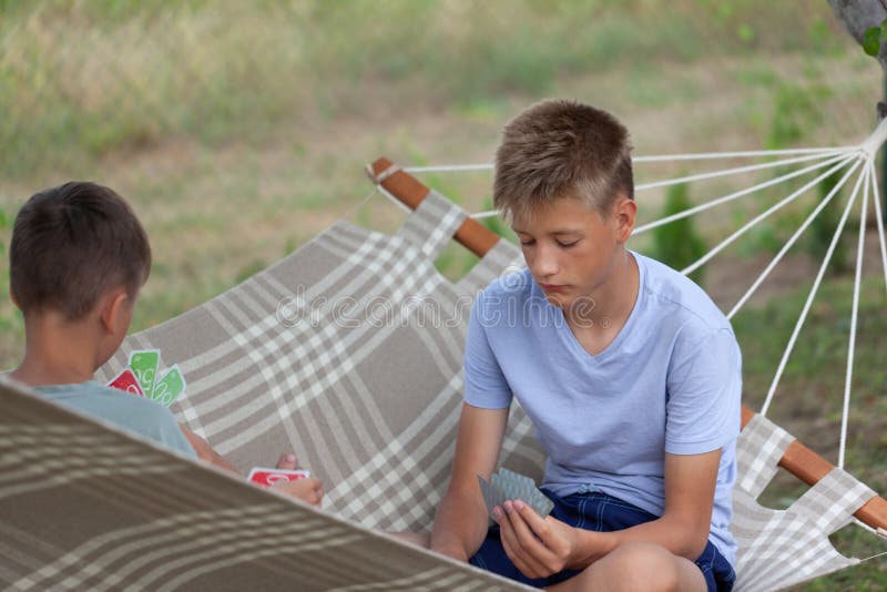 Милые два мальчика братья сидят в гамаке в летний день и играют в карты на улице стоковые изображения