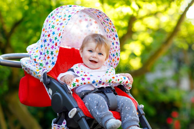 Милый маленький красивый ребёнок 6 месяцев сидя в маме pram или прогулочной коляски и ждать. Милый маленький красивый ребёнок сидя в маме pram или прогулочной коляски и ждать Счастливый усмехаясь ребенок с голубыми глазами С зеленой предпосылкой дерева Дочь младенца идя для прогулки