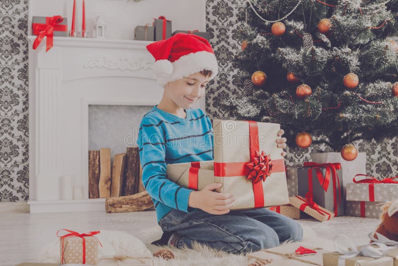 Милый мальчик в шляпе santa развертывая подарки на рождество стоковые изображения rf