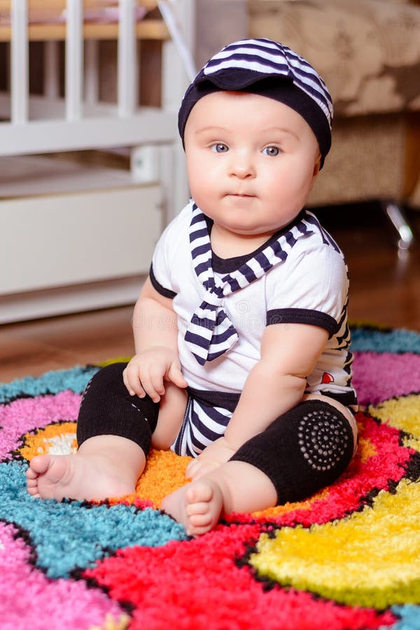 Милый младенец в striped рубашке и шляпах усаженных на циновку в комнате стоковое фото Милый младенец в striped рубашке и шляпах усаженных на циновку в комнате стоковое фото