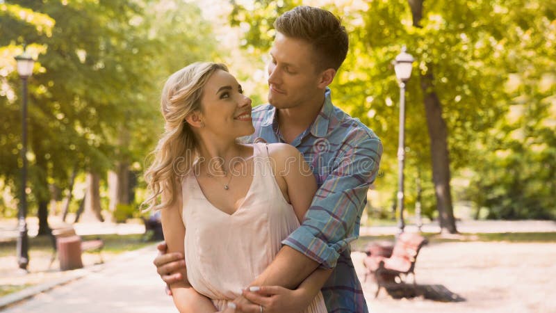 Cute guy and girl looking at each other with love tenderly, cuddling in park, stock footage. Cute guy and girl looking at each other with love tenderly, cuddling in park, stock footage