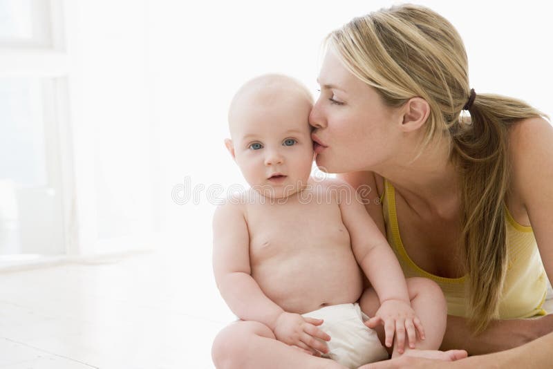 Mother kissing baby indoors at home. Mother kissing baby indoors at home