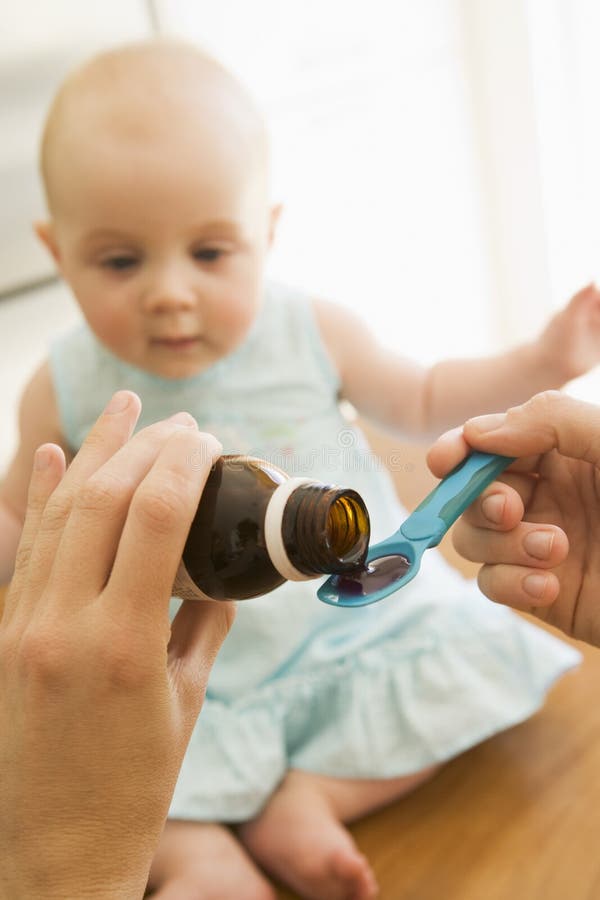 Mother giving baby medicine on a spoon indoors. Mother giving baby medicine on a spoon indoors