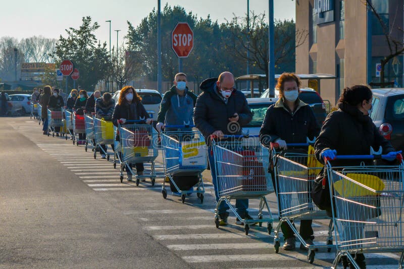 Tuscany, Italy 03/21/20 - Line of italian men and women with coronavirus protective masks waiting with shopping carts to do grocery. National lockdown, anxious people fear shortages. Food and basic needs available after long wait in a line, daily routine in epidemic Covid19. Tuscany, Italy 03/21/20 - Line of italian men and women with coronavirus protective masks waiting with shopping carts to do grocery. National lockdown, anxious people fear shortages. Food and basic needs available after long wait in a line, daily routine in epidemic Covid19