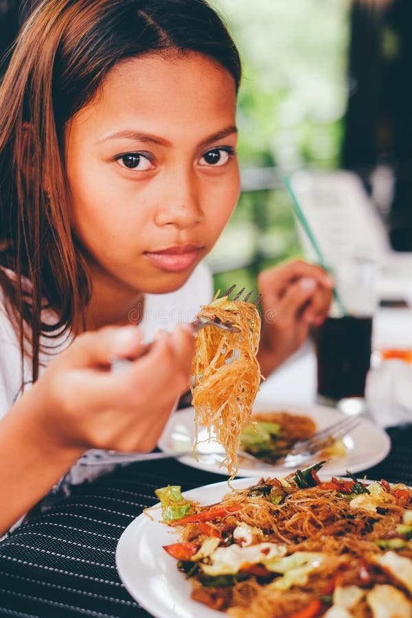 Young Asian woman at the restaurant eating stir fry rice noodle with meat and vegetables, Philippine food call pansit bihon. Young Asian woman at the restaurant eating stir fry rice noodle with meat and vegetables, Philippine food call pansit bihon.