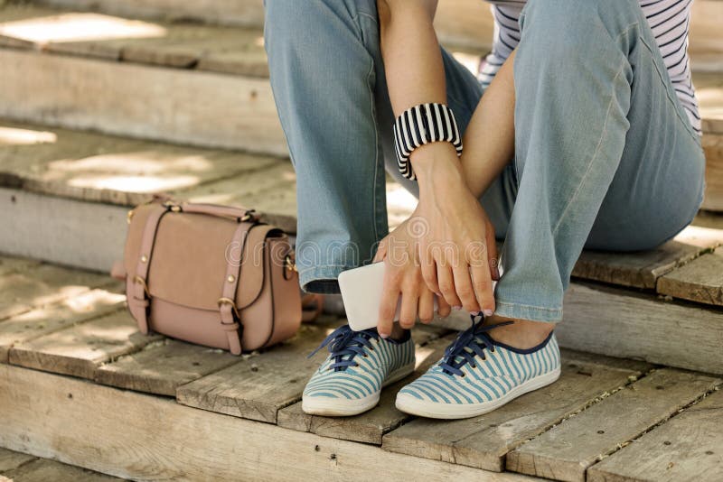 Молодая женщина в голубых джинсах и striped тапках сидит на старом woode стоковые фотографии rf