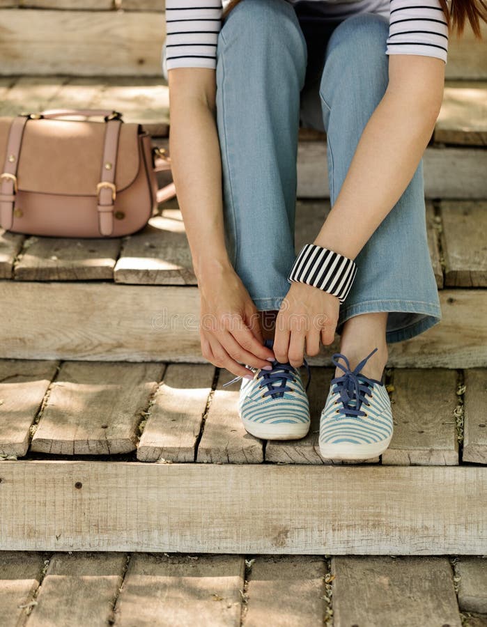 Молодая женщина в голубых джинсах и striped тапках сидит на старом woode стоковые фото