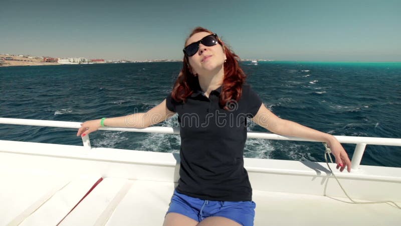 Молодая женщина в солнечных очках сидит на усмехаться шлюпки яхты