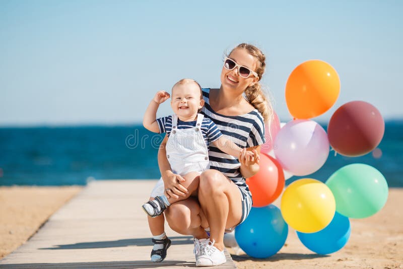 The happy family relaxing near the sea young mother with the little son, are dressed in striped t-shirts and white shorts, sun glasses, have fun together on a sandy beach on a wooden path against the clear blue sky and the blue sea. The happy family relaxing near the sea young mother with the little son, are dressed in striped t-shirts and white shorts, sun glasses, have fun together on a sandy beach on a wooden path against the clear blue sky and the blue sea.