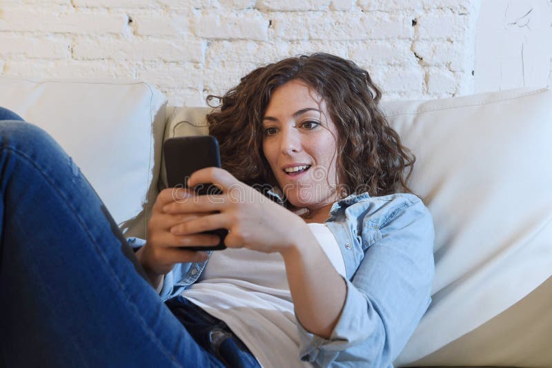 Молодая привлекательная испанская женщина используя мобильный телефон app или отправляющ СМС на домашнем кресле стоковая фотография rf