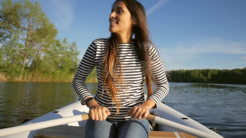 Молодая счастливая девушка смешанной гонки гребя раздувную шлюпку с деревянными веслами на озере Отснятый видеоматериал образа жи