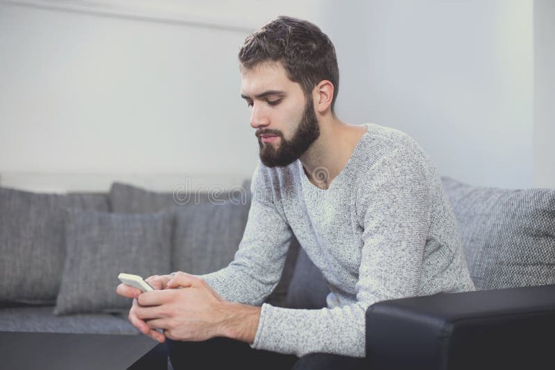 Молодое вскользь послание человека на smartphone на софе стоковые изображения rf Молодое вскользь послание человека на smartphone на софе стоковые изображения rf